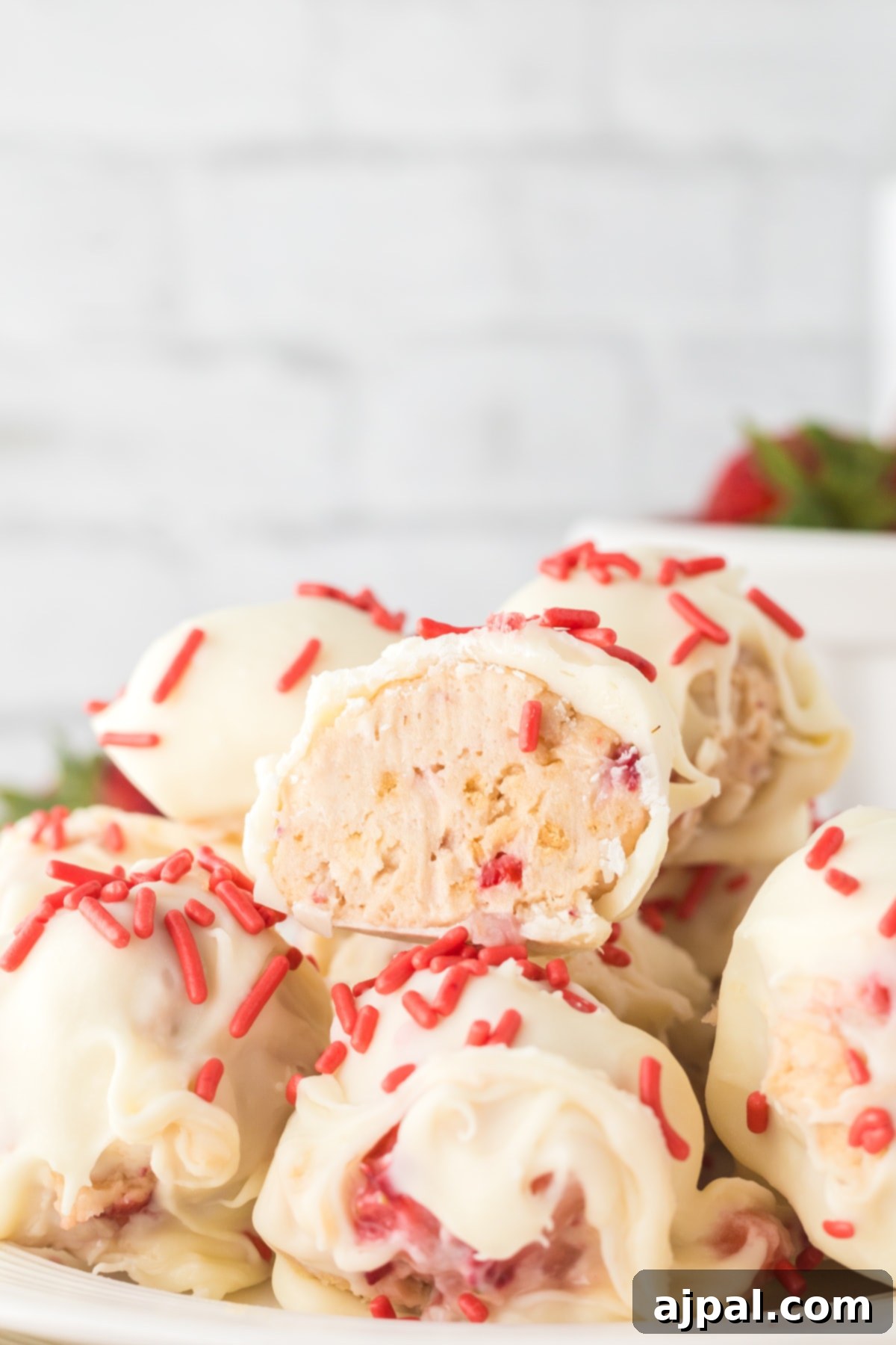A stack of delightful strawberry shortcake truffles, dipped in white chocolate and finished with festive pink sprinkles, arranged on a white plate for a stunning presentation.