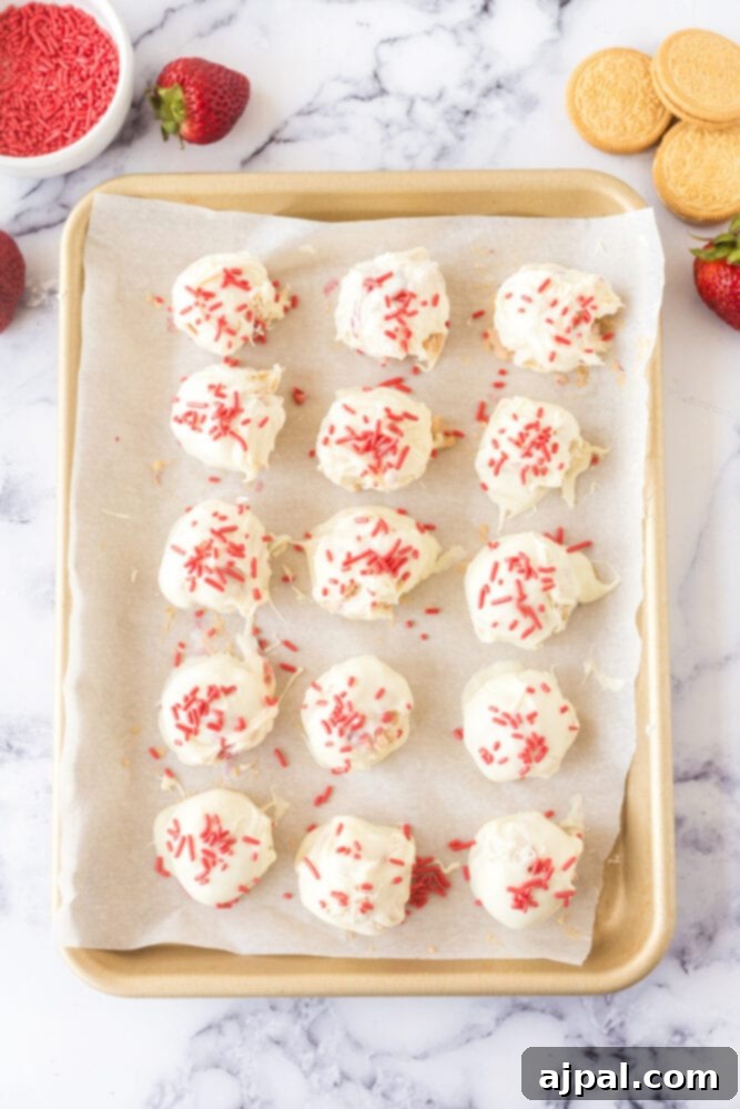 White chocolate-dipped truffles, freshly coated and adorned with sprinkles, are lined up on a parchment-lined baking sheet for chilling.