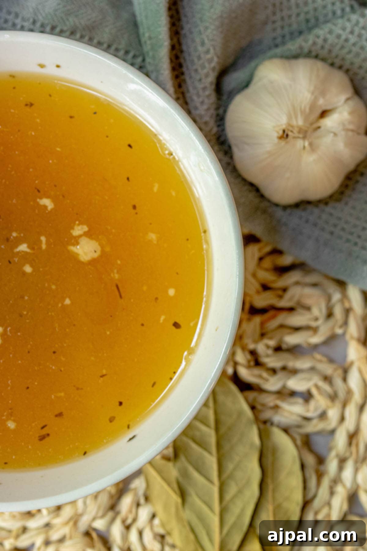 Homemade Slow Cooker Turkey Stock 3 A rustic bowl filled with golden slow cooker turkey stock, garnished with bay leaves and garlic cloves, set against a blurred background, suggesting warmth and comfort.