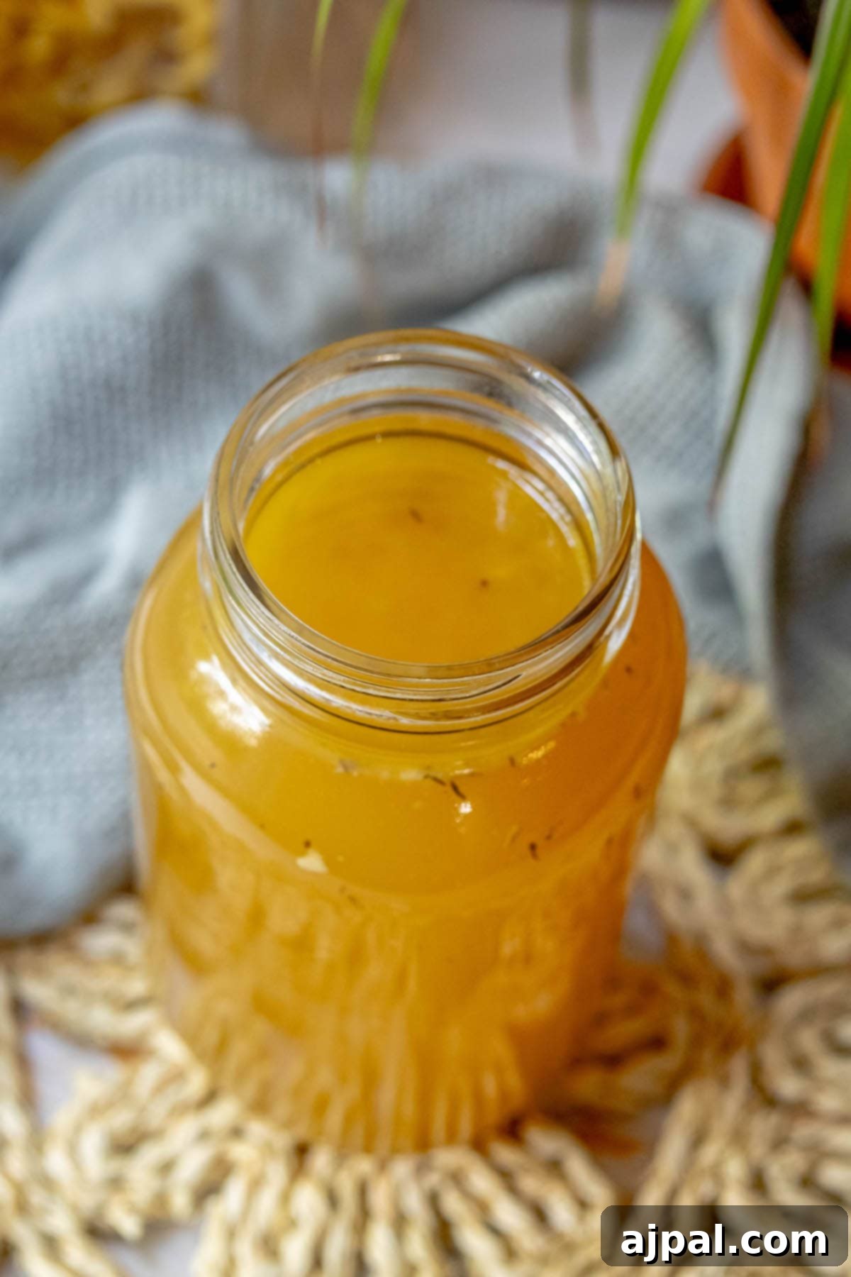 Homemade Slow Cooker Turkey Stock 4 A glass jar filled with yellow turkey stock sits on a wooden table, next to a small green plant, emphasizing its natural, wholesome preparation.