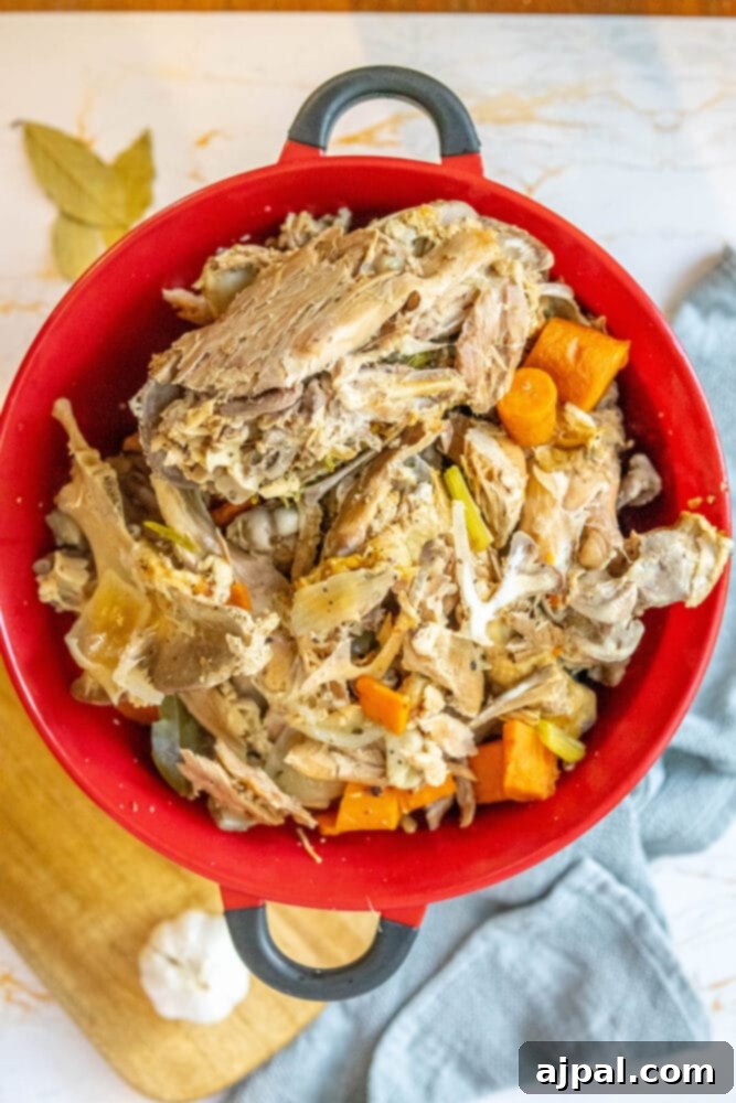 Homemade Slow Cooker Turkey Stock 6 Cooked turkey carcass and vegetables in a colander over a bowl, illustrating the straining process for homemade turkey stock.