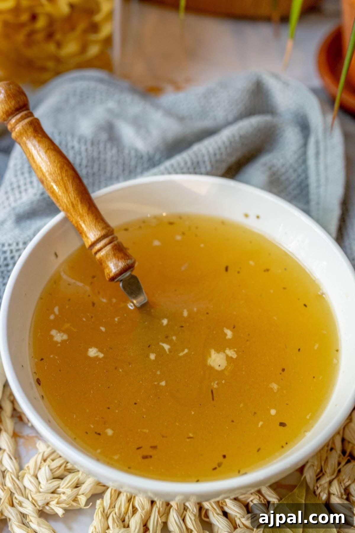 Homemade Slow Cooker Turkey Stock 7 A bowl of rich yellow turkey stock with a wooden spoon rests on a rustic surface, inviting a comforting culinary experience.