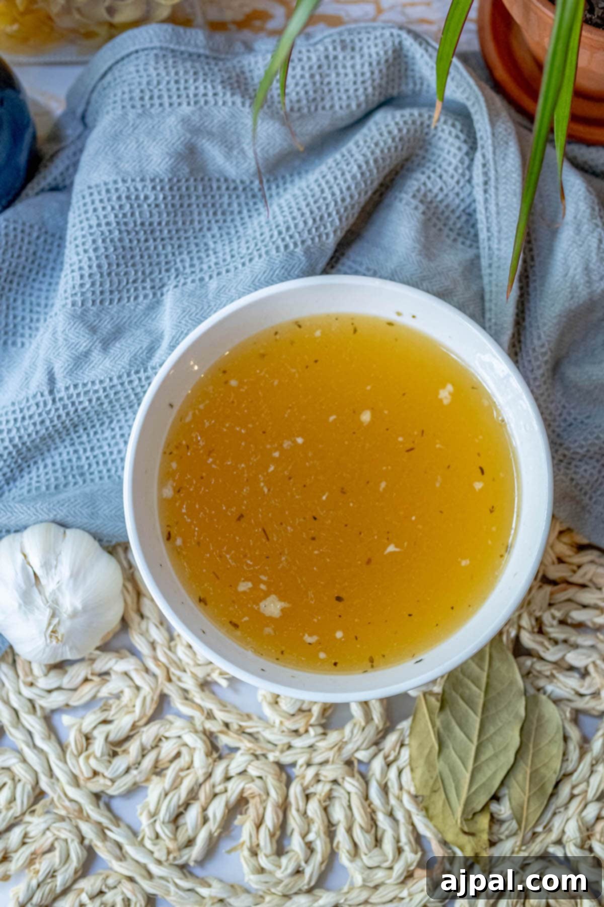 Homemade Slow Cooker Turkey Stock 8 A bowl of vibrant yellow turkey stock, infused with garlic and herbs, rests delicately on a lace doily, symbolizing its nourishing and comforting qualities.