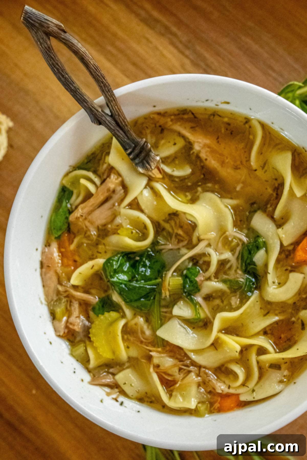 Hearty Slow Cooker Turkey Noodle Soup 2 A bowl of slow cooker turkey noodle soup, filled with egg noodles, tender turkey, vibrant spinach, carrots, and celery, served on a wooden table.