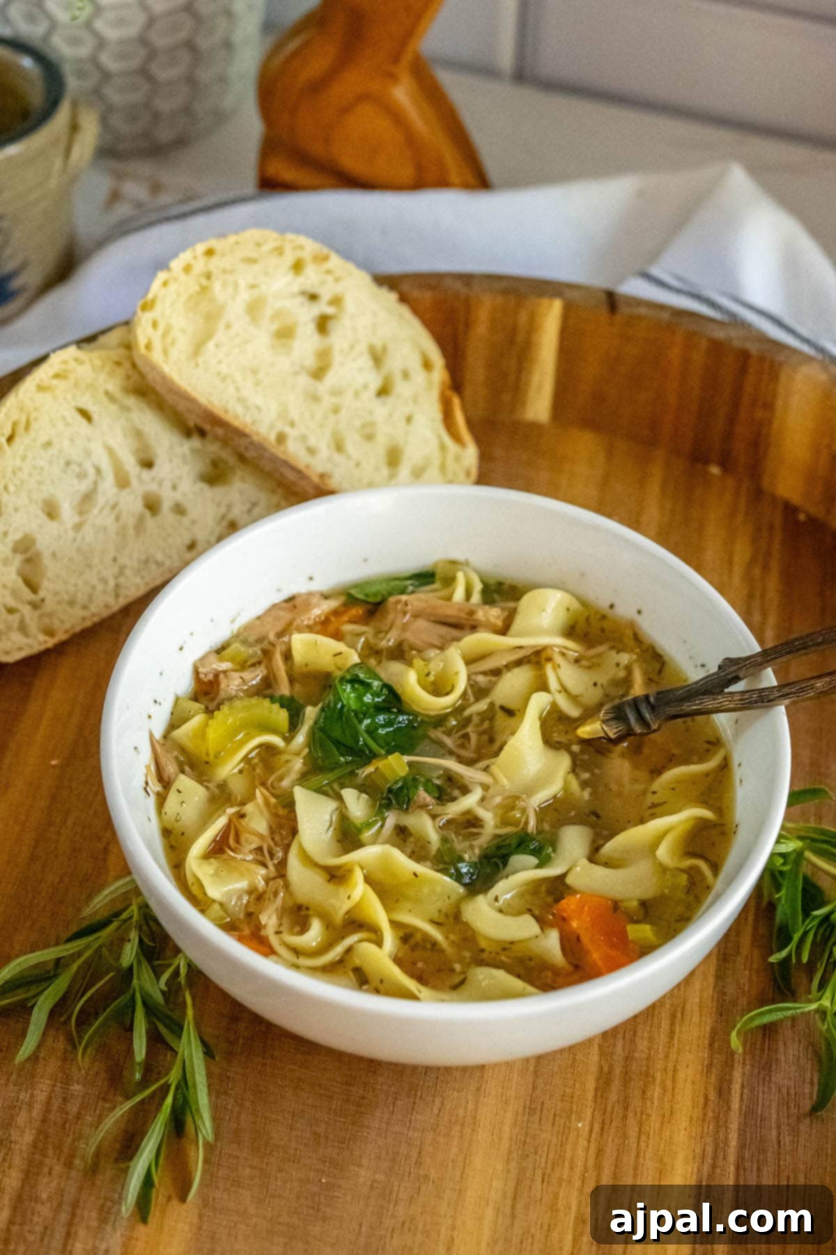 Hearty Slow Cooker Turkey Noodle Soup 4 A serving of slow cooker turkey noodle soup, showcasing the delightful mix of egg noodles, turkey, spinach, carrots, and celery in a savory stock, presented in a bowl on a wooden cutting board.