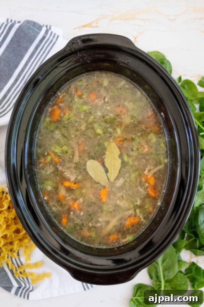 Hearty Slow Cooker Turkey Noodle Soup 8 A slow cooker filled with rich stock, carrots, celery, and bay leaves, simmering gently to create a flavorful base for the turkey noodle soup.