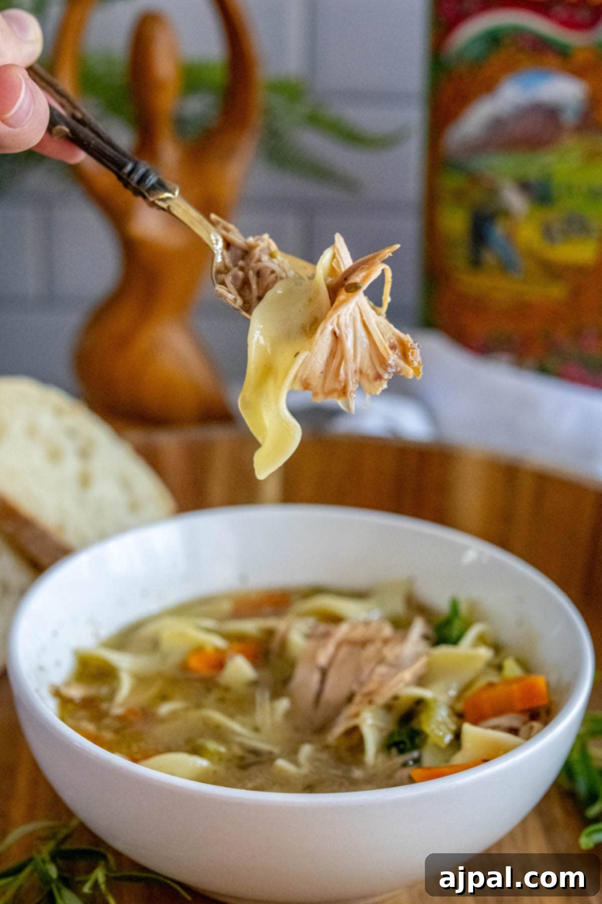 Hearty Slow Cooker Turkey Noodle Soup 9 A generous serving of slow cooker turkey noodle soup, with egg noodles, turkey, spinach, carrots, and celery visible in a bowl, and a spoon full of noodles and turkey poised above it.