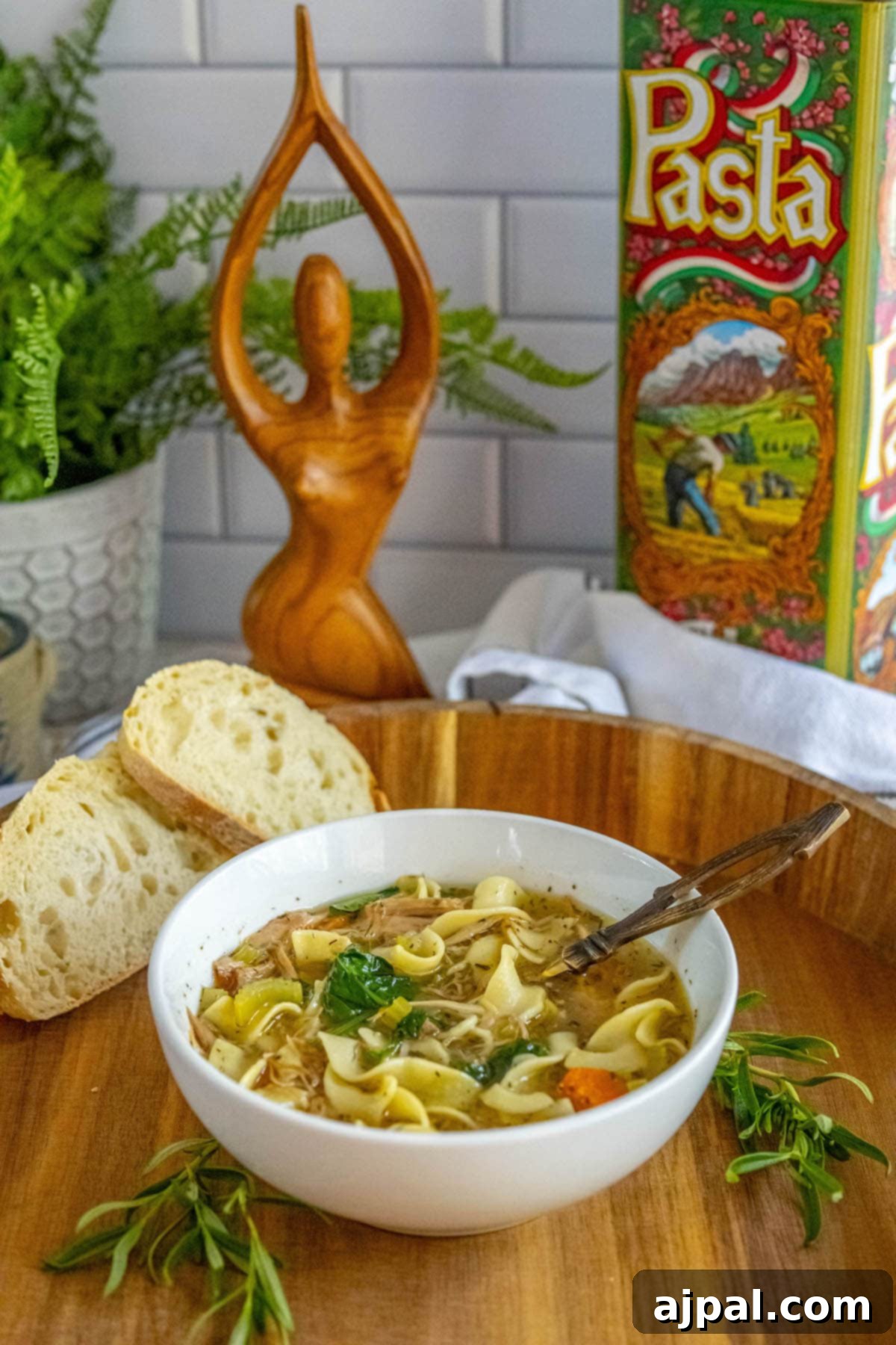 Hearty Slow Cooker Turkey Noodle Soup 10 A bowl of slow cooker turkey noodle soup, rich with egg noodles, turkey, spinach, carrots, and celery, served invitingly on a wooden cutting board.
