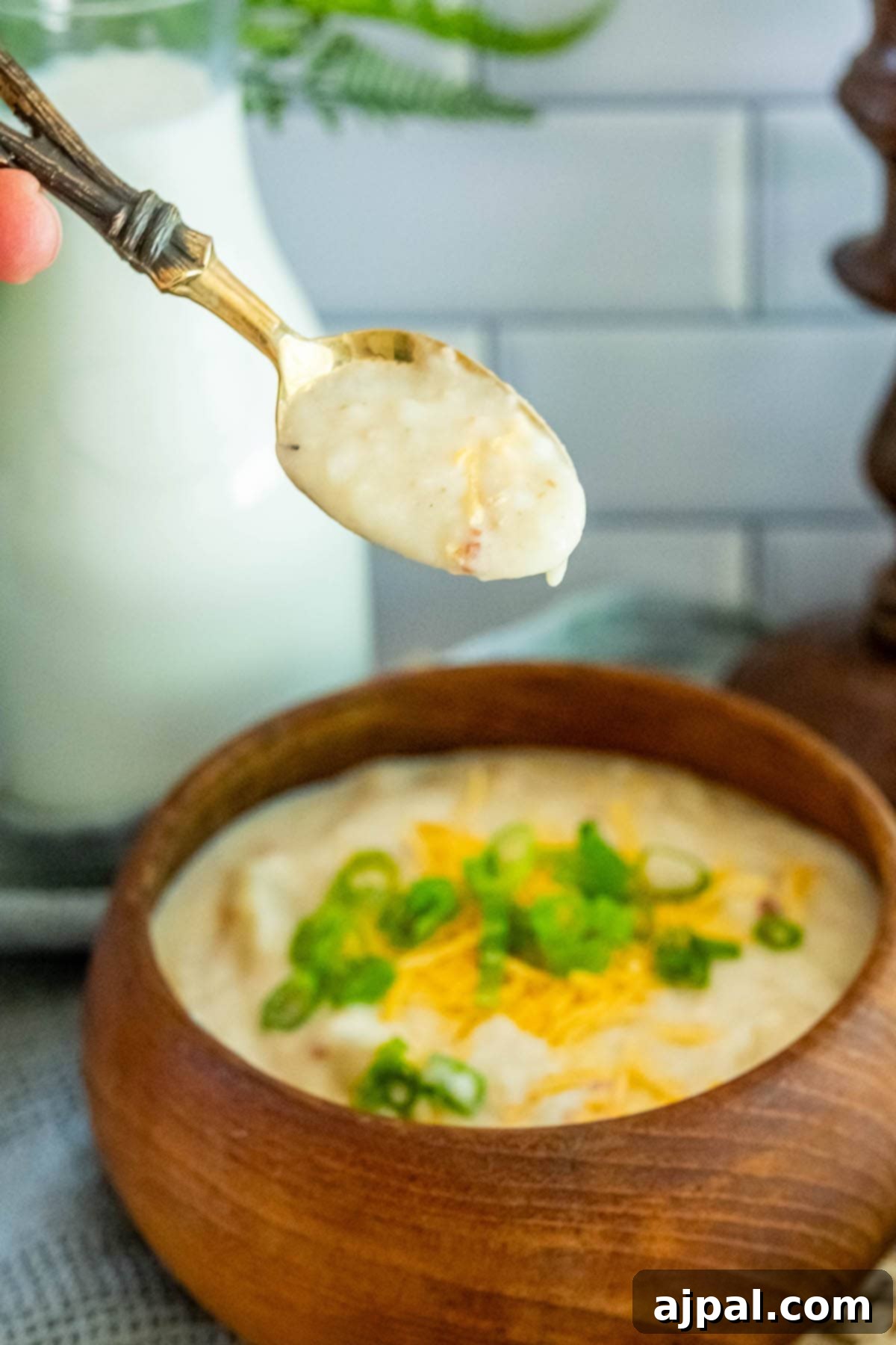 Creamy Slow Cooker Loaded Baked Potato Soup 4 A spoonful of slow cooker potato soup being lifted from a rustic wooden bowl, showcasing its creamy consistency