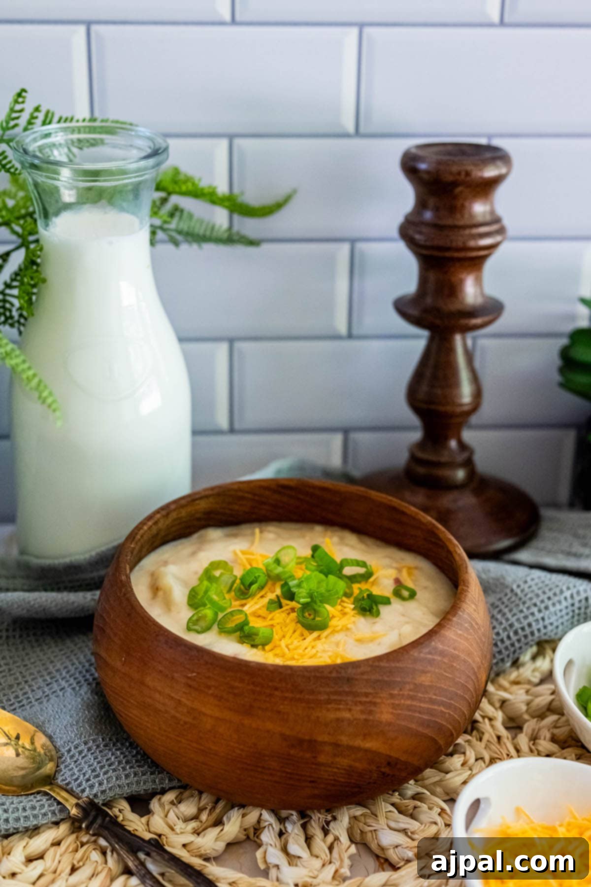 Creamy Slow Cooker Loaded Baked Potato Soup 10 A bowl of slow cooker loaded cheesy potato soup on a wooden table, next to a glass of milk