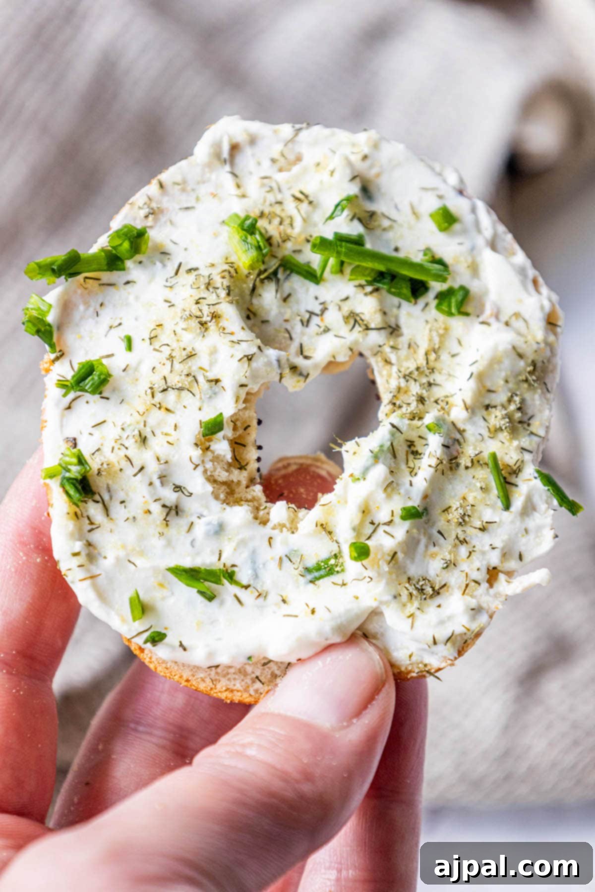 A hand holding an everything bagel generously covered with creamy garlic dill schmear.