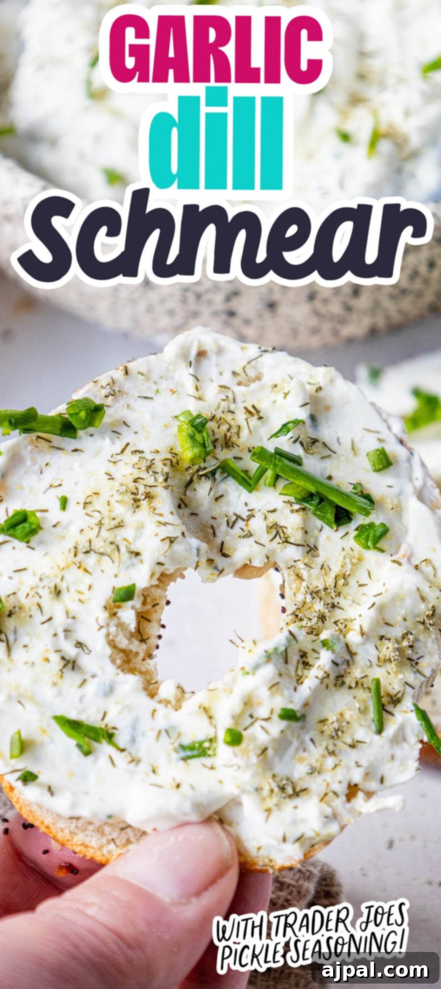 A hand holding an everything bagel generously covered with creamy garlic dill schmear, ready to be enjoyed.