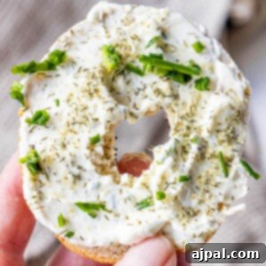 A hand holding an everything bagel with garlic dill schmear all over it