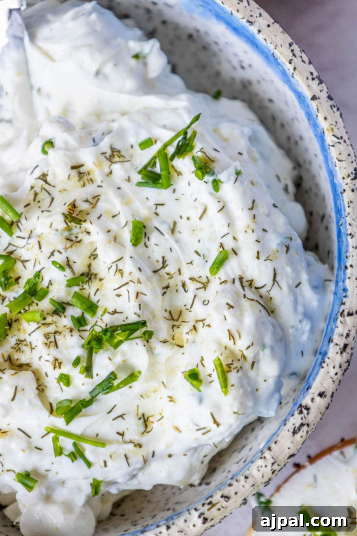 A bowl of creamy dill schmear, garnished with chopped chives and a sprinkle of pickle seasoning, ready to be served.
