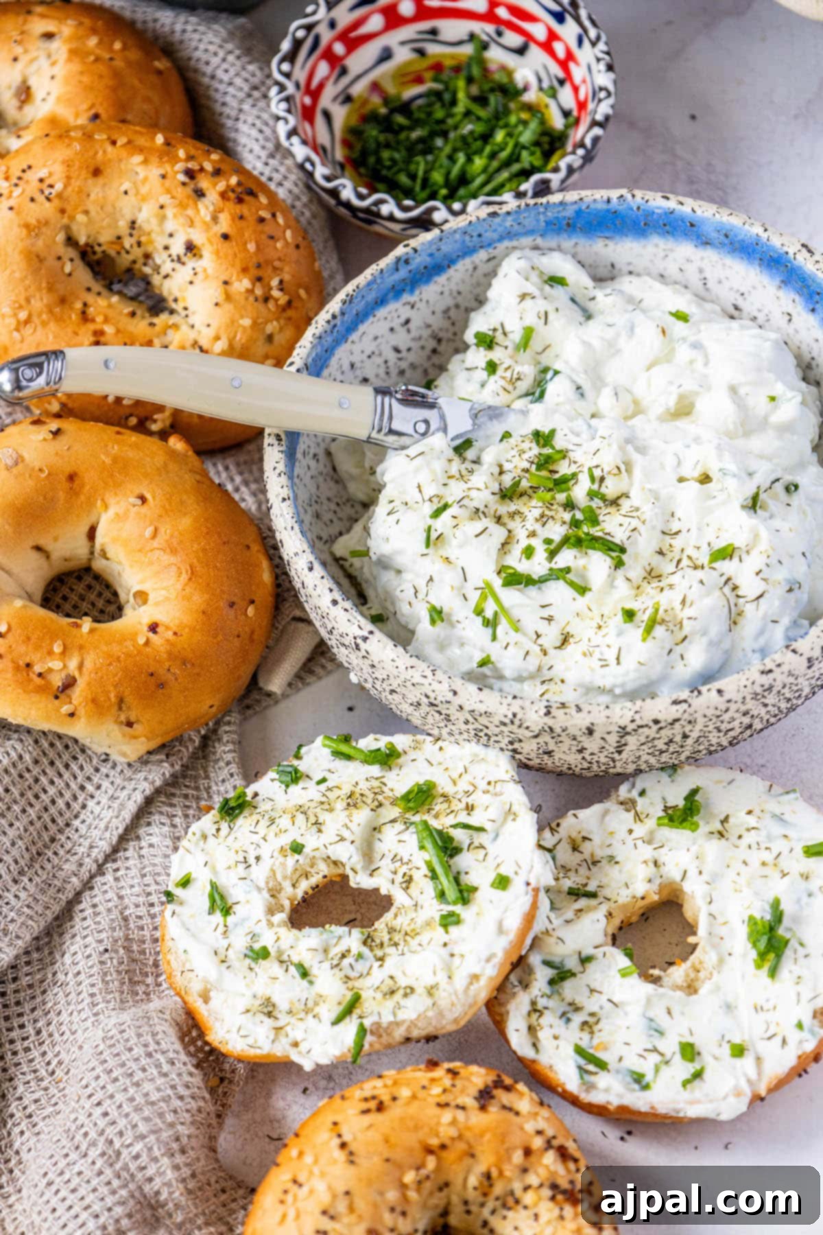 A selection of everything bagels generously topped with garlic dill schmear, fresh chives, and pickle seasoning, arranged on a rustic table.