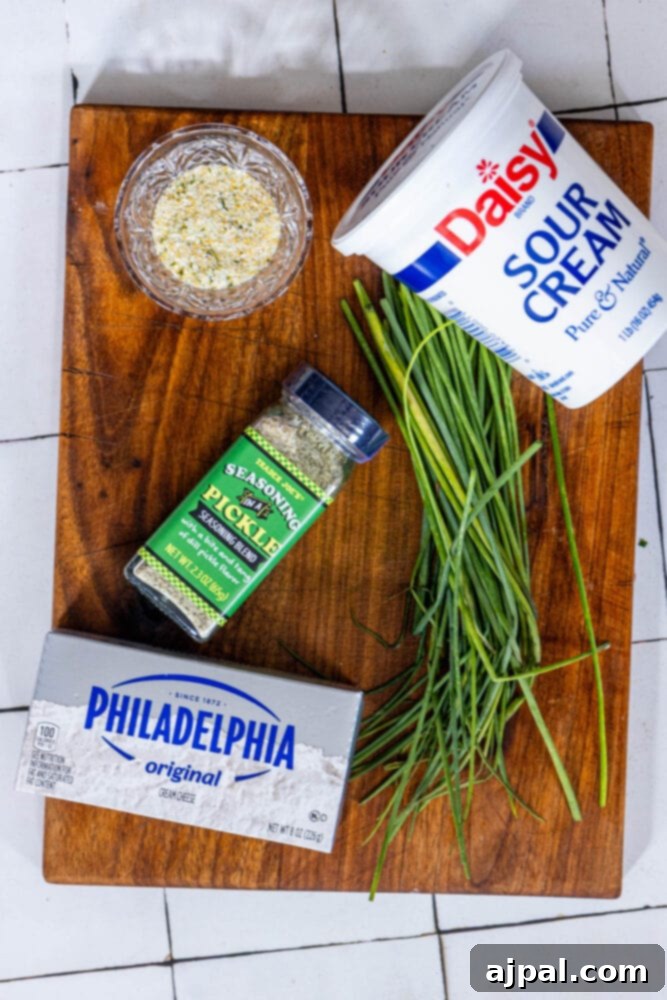 An array of ingredients for garlic dill schmear laid out on a cutting board, including garlic powder, sour cream, cream cheese, and pickle seasoning.