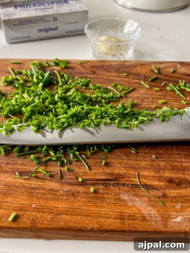 Freshly chopped chives neatly piled on a wooden cutting board, ready for use.
