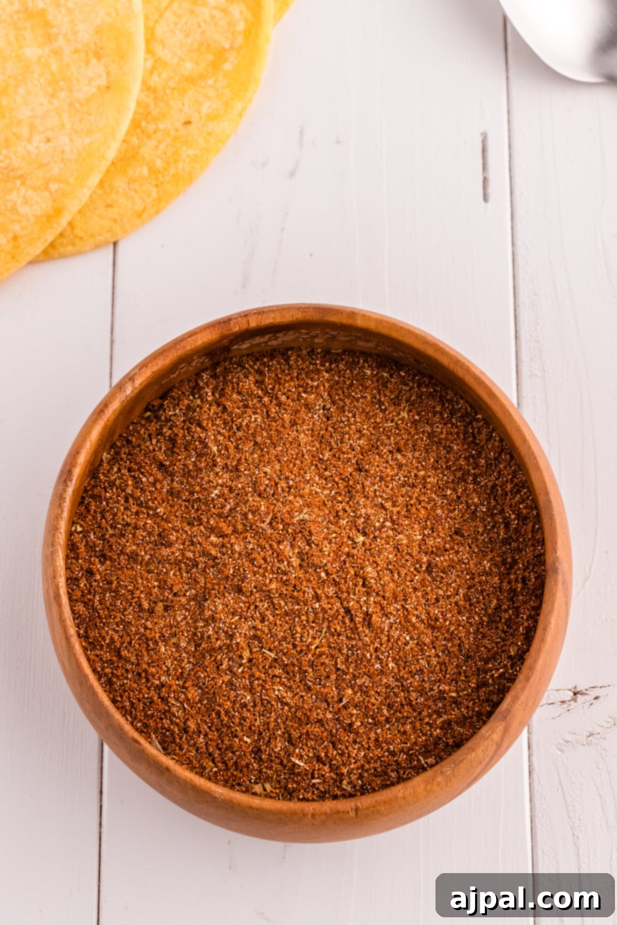 Taco Spice Blend 4 Homemade taco seasoning in a small white bowl on a wooden table, with a spoon nearby