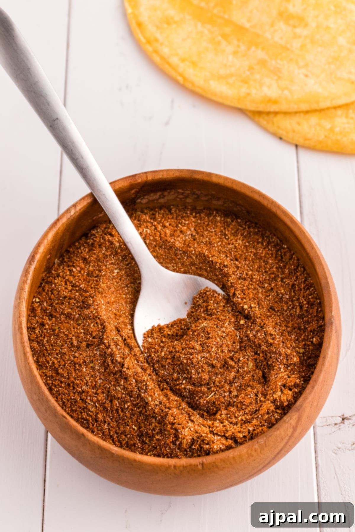 Taco Spice Blend 7 A wooden spoon scooping homemade taco seasoning from a larger bowl, showing its rich texture and color