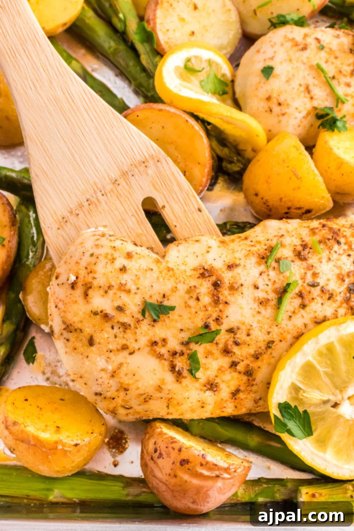A close-up view of a baked sheet pan dinner, highlighting the perfectly cooked lemon garlic chicken breasts, roasted potatoes, and asparagus.