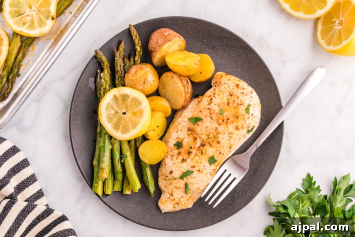 A beautifully plated serving of sheet pan lemon garlic chicken, asparagus, and potatoes on a black plate, showcasing the golden-brown chicken and vibrant vegetables.