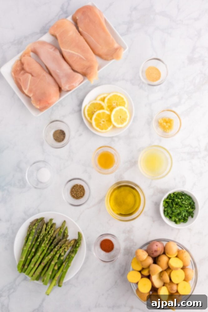 Raw chicken, honey, olive oil, spices, fresh asparagus, and baby potatoes laid out on a table, ready for preparation.