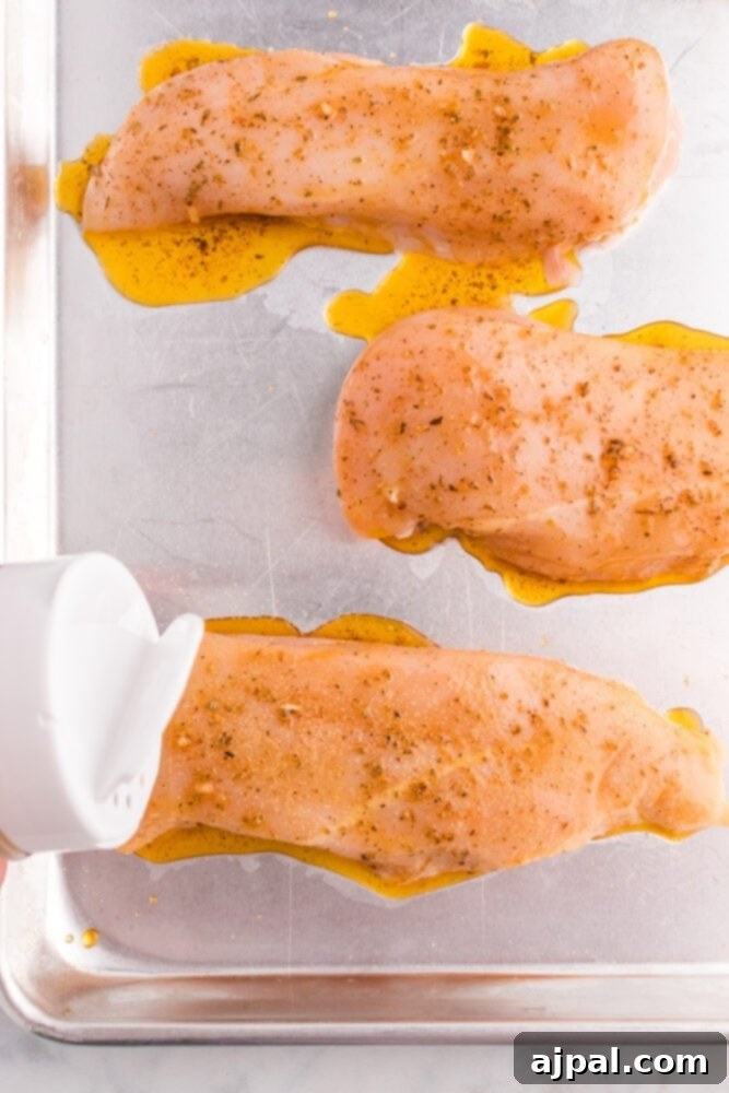 Raw chicken breasts being seasoned directly on a baking sheet, preparing for the lemon garlic marinade.