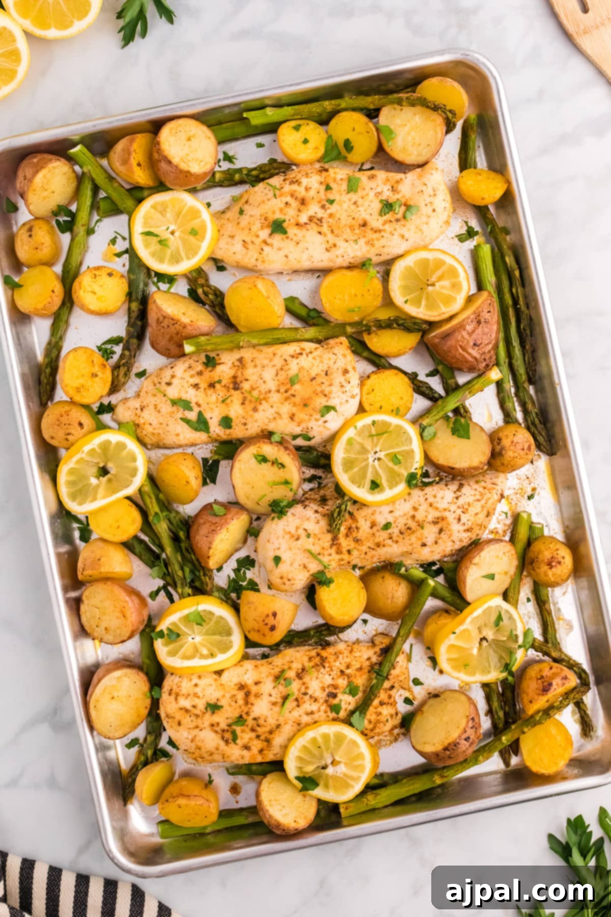 A sheet pan fresh out of the oven, laden with baked lemon garlic chicken breasts, golden roasted potatoes, tender asparagus, and caramelized lemon slices.