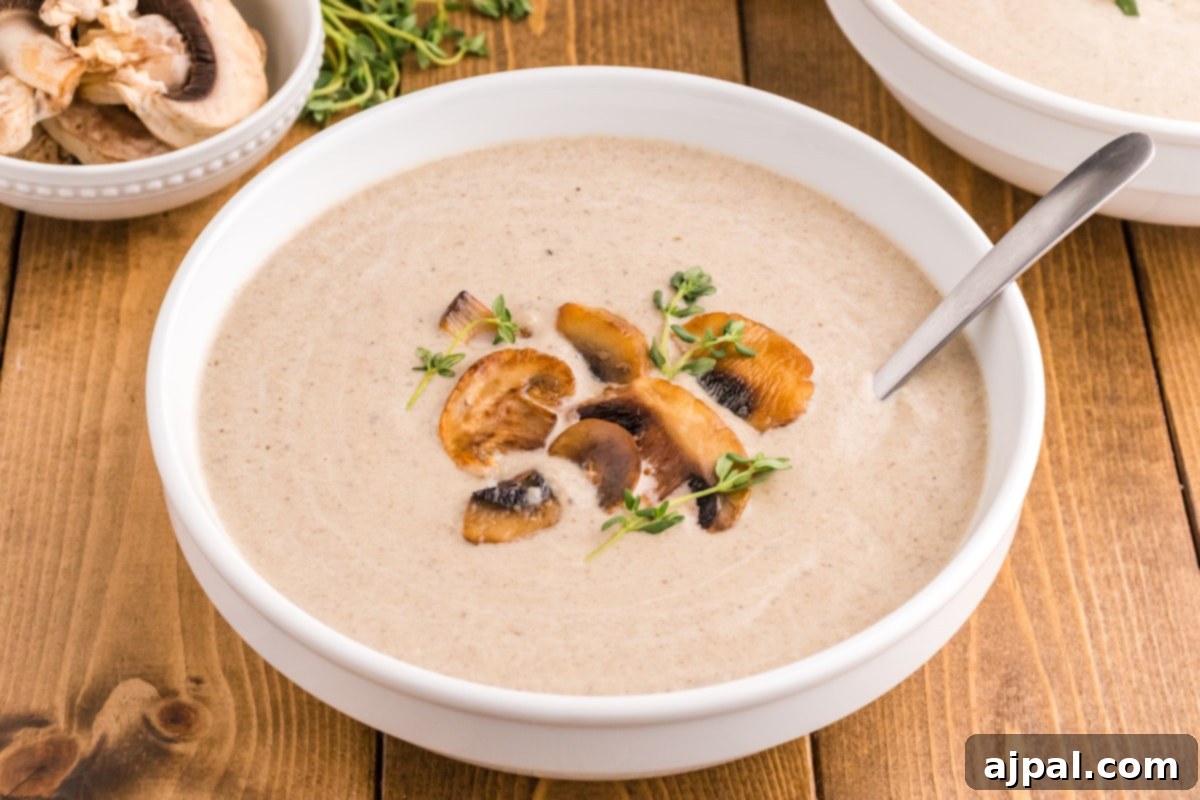 a spoon with mushroom soup and roasted mushrooms on it in a bowl of mushroom soup topped with fresh thyme