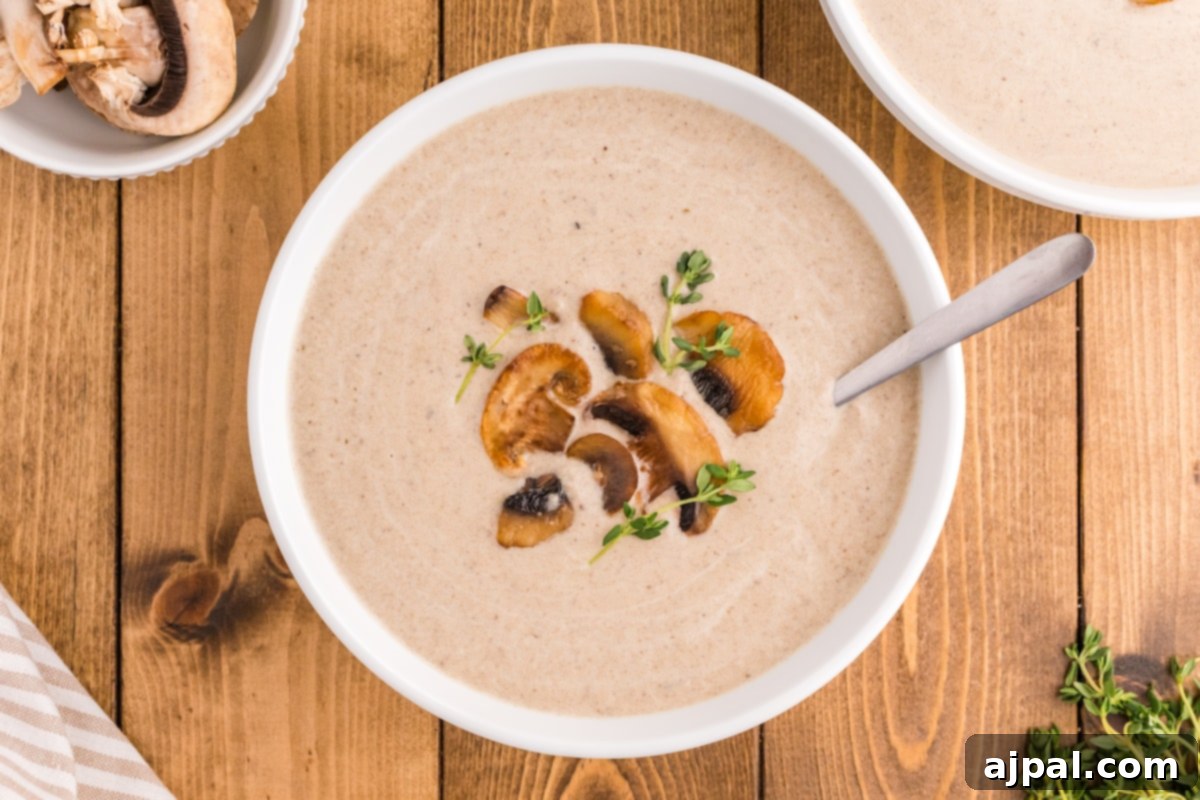 a spoon with mushroom soup and roasted mushrooms on it in a bowl of mushroom soup topped with fresh thyme