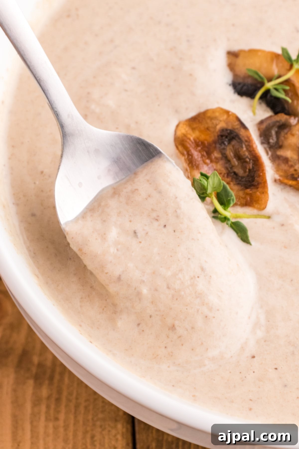 a spoon with mushroom soup and roasted mushrooms on it in a bowl of mushroom soup topped with fresh thyme