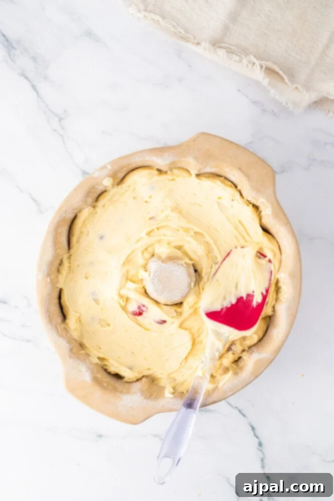 Bright Cranberry Orange Bundt Cake 11 A rich, orange-hued cake batter being gently mixed in a bowl, showing its smooth consistency.