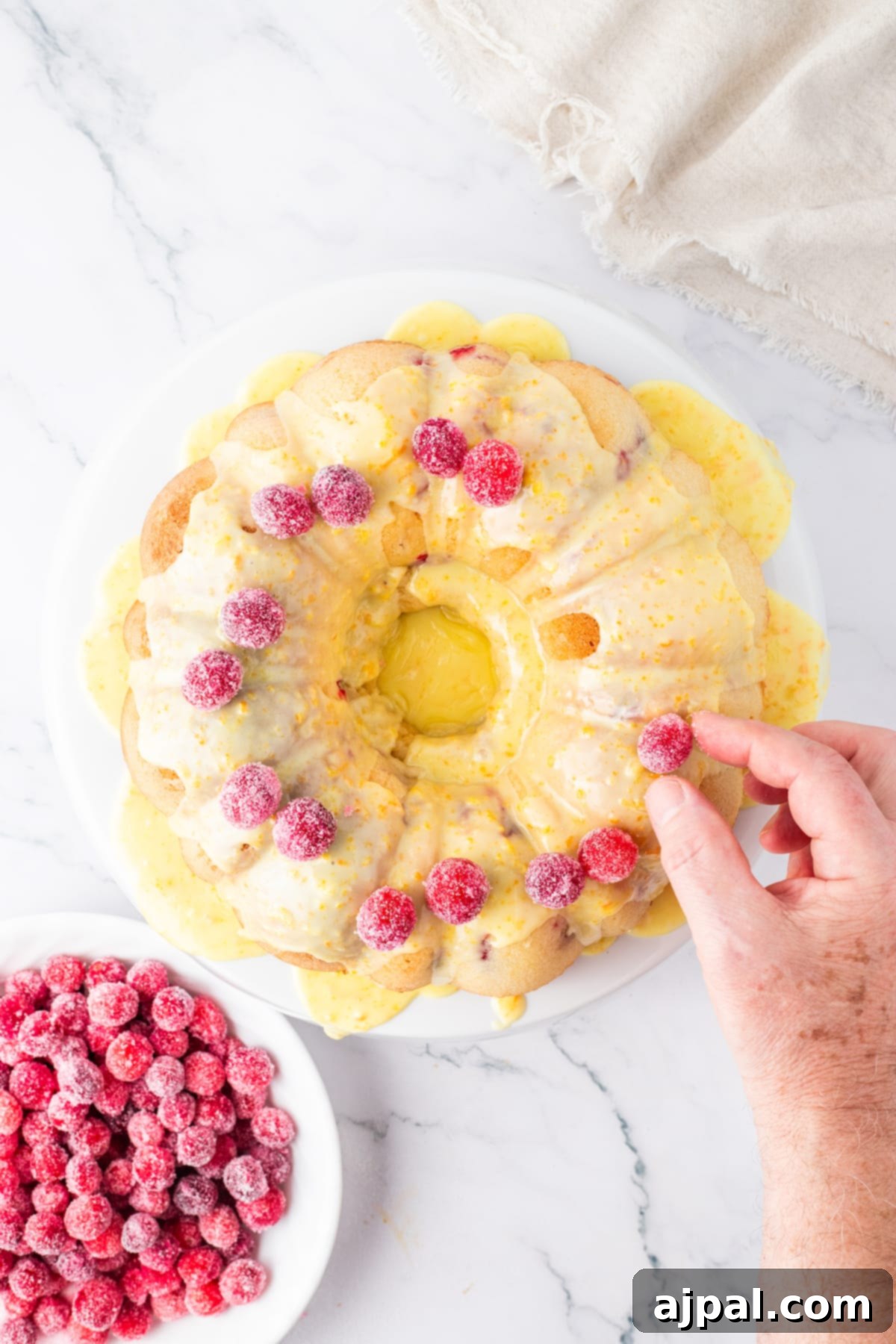 Bright Cranberry Orange Bundt Cake 15 A hand carefully garnishing a Cranberry Orange Bundt Cake with fresh raspberries, enhancing its festive appeal.
