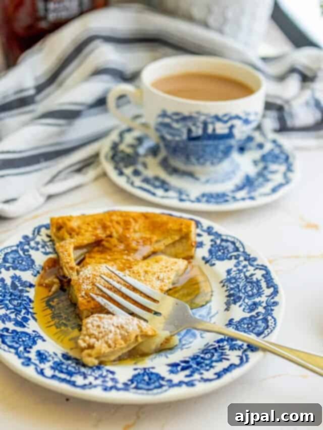 A delectable slice of Cinnamon Apple Dutch Baby on a blue and white plate, ready to be enjoyed with a hot cup of coffee.