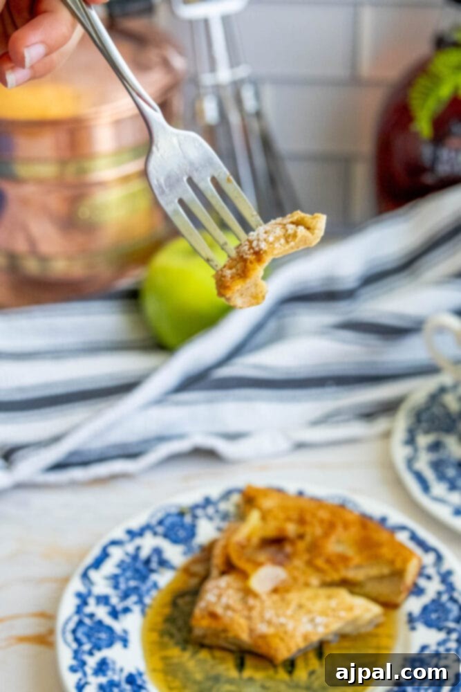 A close-up shot of a fork gently lifting a piece of Cinnamon Apple Dutch Baby, highlighting its fluffy texture and apple chunks.