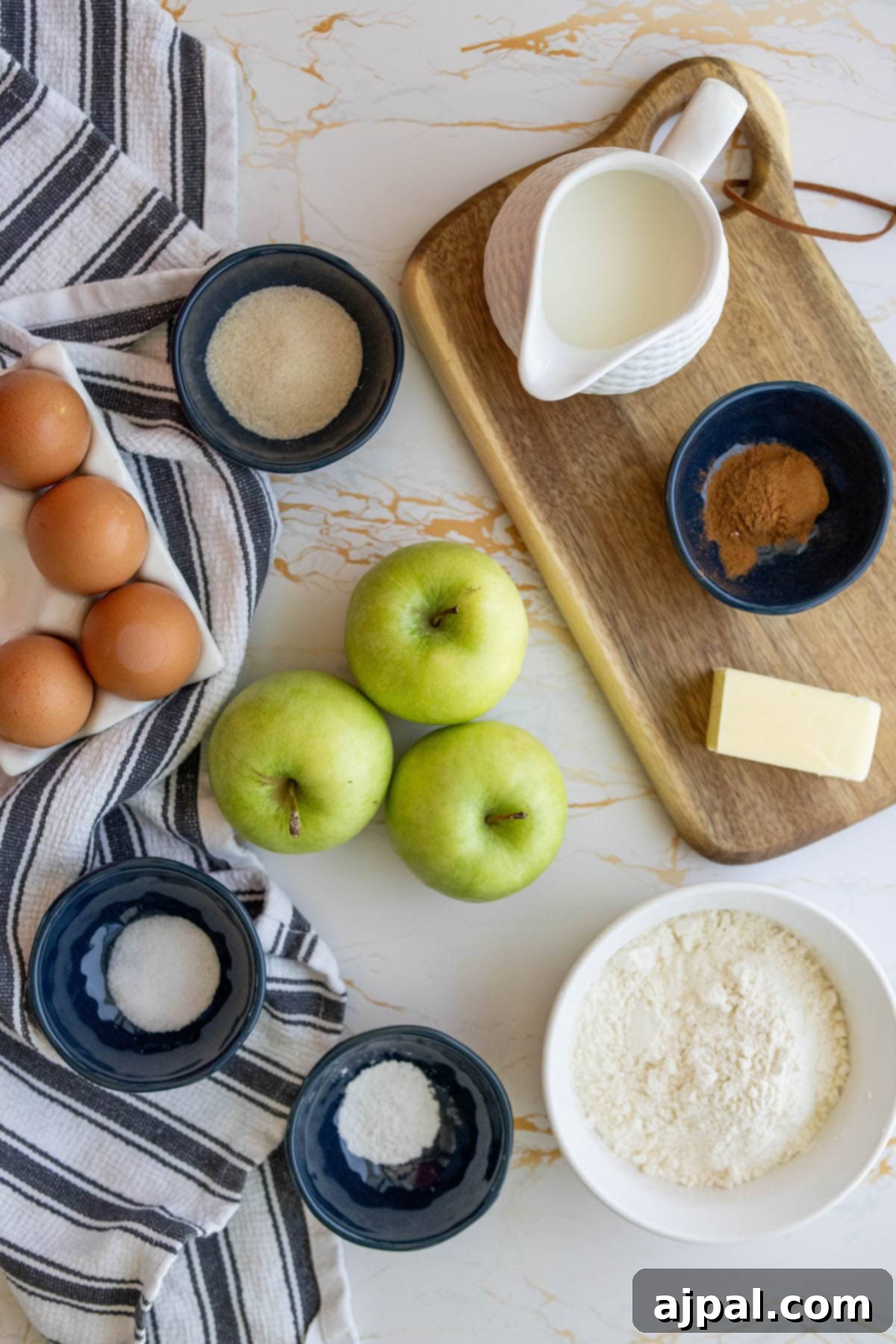 A collection of fresh baking ingredients including vibrant green apples, cinnamon sticks, eggs, flour, and baking powder, laid out in separate containers ready for the Dutch baby recipe.