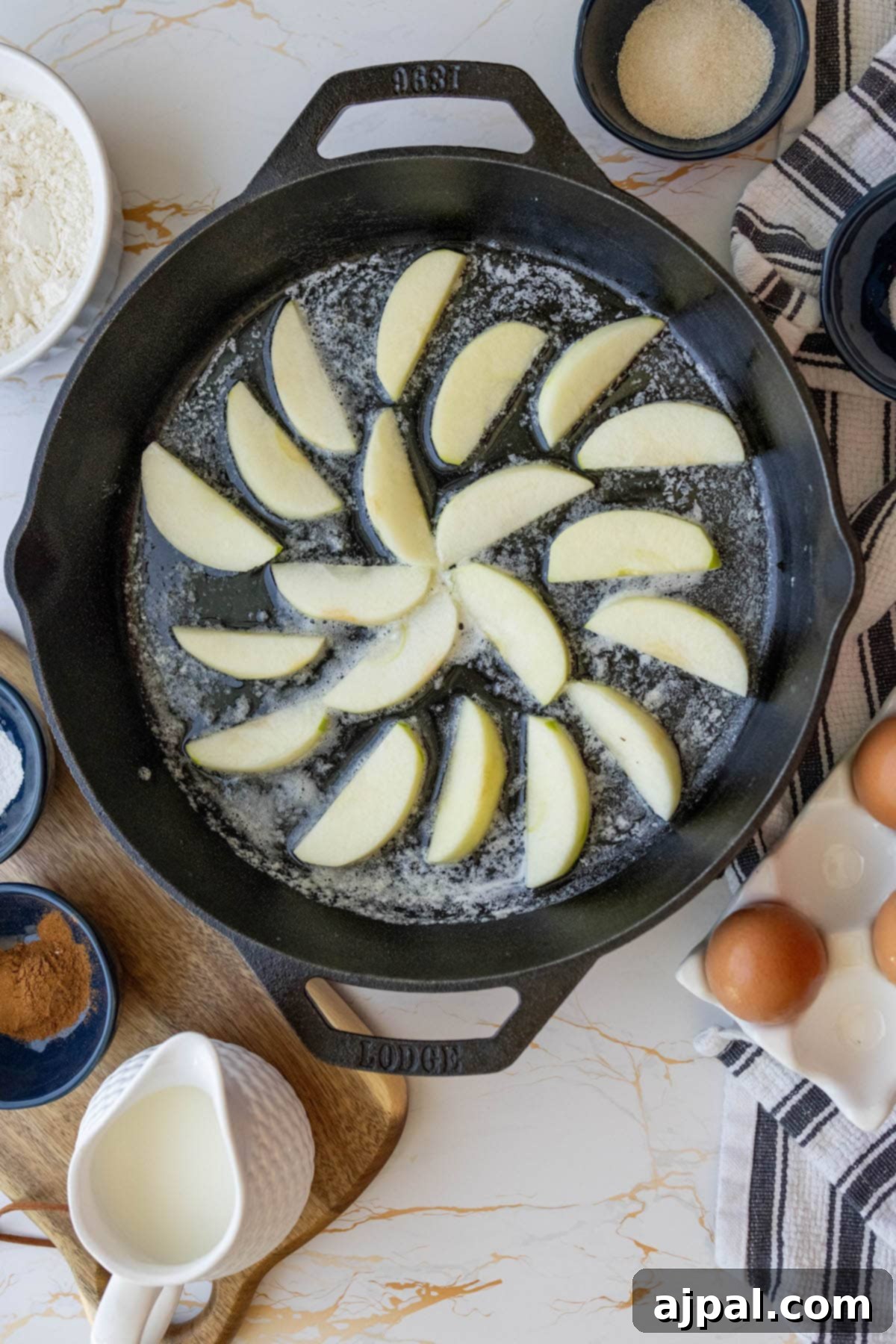 Delicately arranged thin slices of Granny Smith apples forming a beautiful pattern at the bottom of a hot cast iron skillet, lightly sautéed in butter.