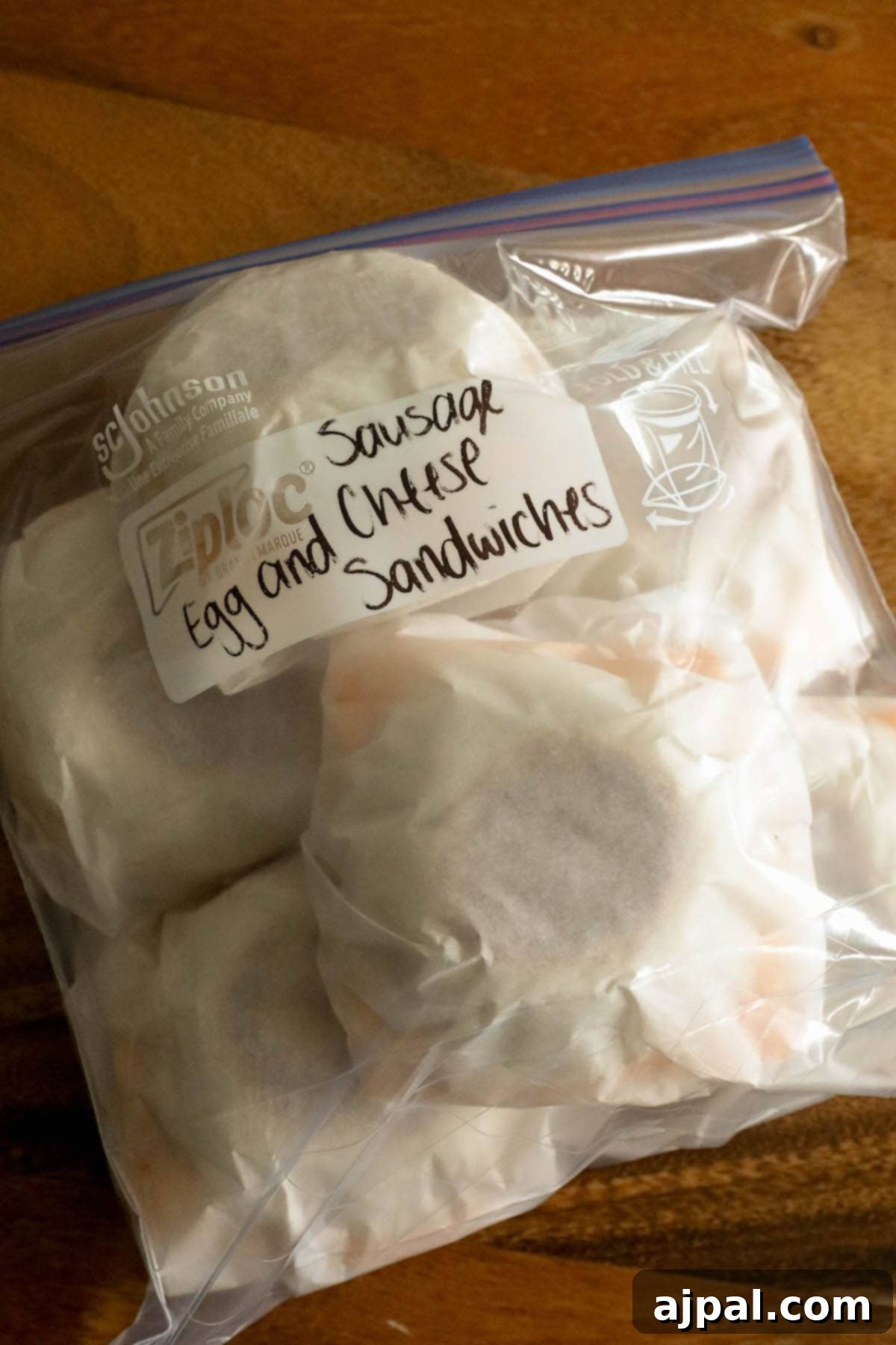 Grab-and-Go Egg Muffin Sandwiches 13 A transparent freezer bag filled with individually wrapped homemade sausage egg muffins, clearly labeled and ready for convenient storage. The sandwiches peek through the parchment paper, showcasing their delicious fillings.