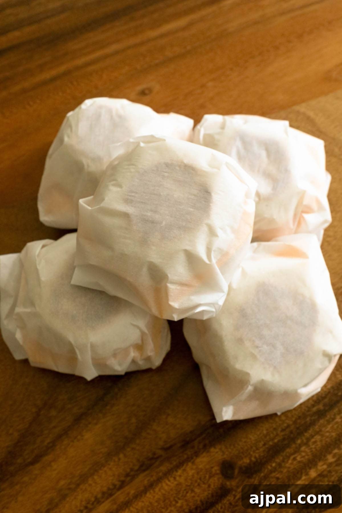 Grab-and-Go Egg Muffin Sandwiches 3 A stack of individually wrapped homemade freezer breakfast sandwiches, nestled in parchment paper, ready for freezing. They are neatly arranged on a wooden table, highlighting their meal prep potential.