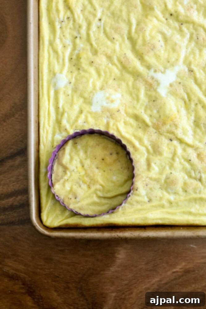 Grab-and-Go Egg Muffin Sandwiches 7 A large, baked egg patty in a sheet pan, with a round cookie cutter pressed into it, demonstrating how to create perfectly sized egg rounds for English muffin sandwiches.