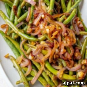 Sautéed green beans and red onion on a white plate.