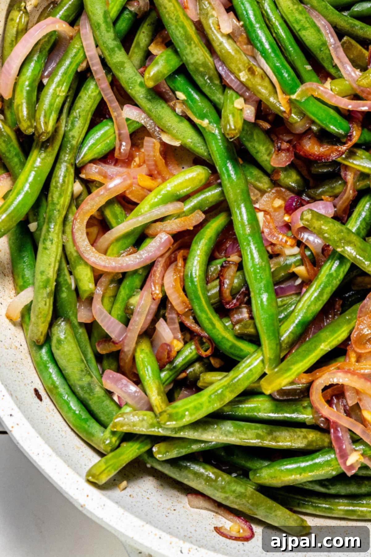 Sautéed green beans and red onion in a skillet.