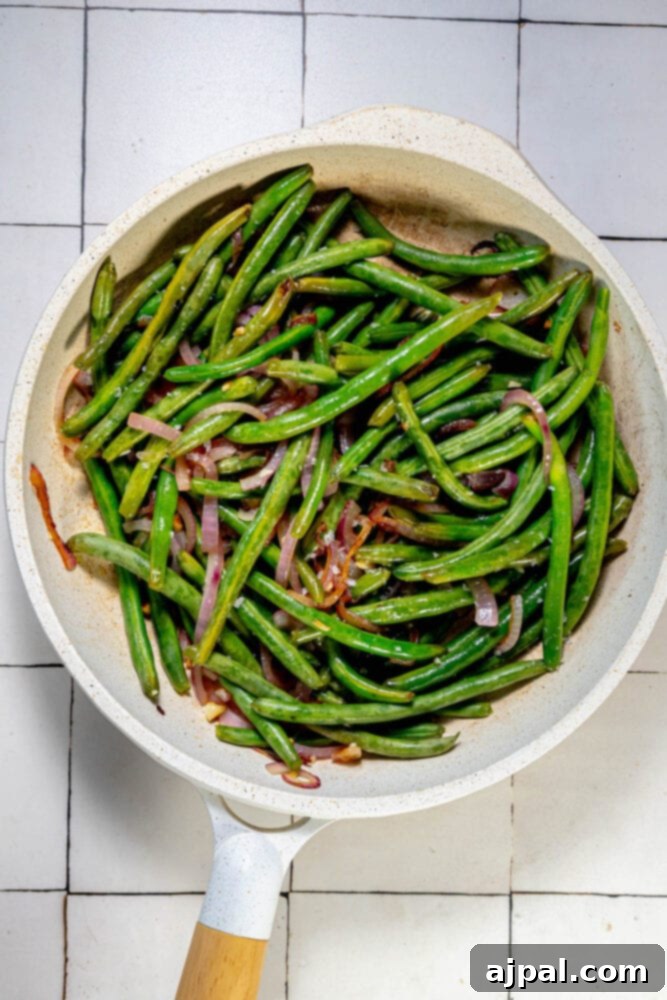 Sautéed green beans and red onion in a skillet.
