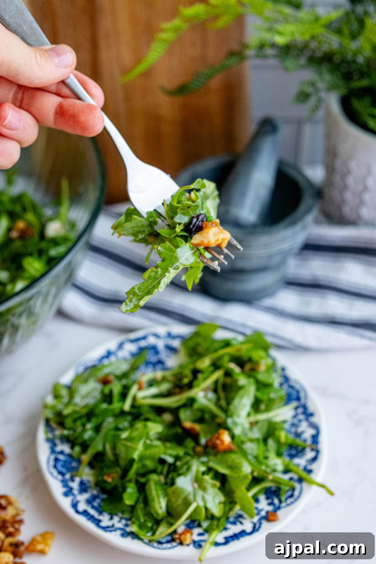 A person is holding a fork over a plate of Arugula Salad, ready to enjoy.