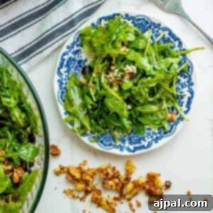 A bowl of arugula salad with walnuts, cranberries, and gorgonzola cheese.