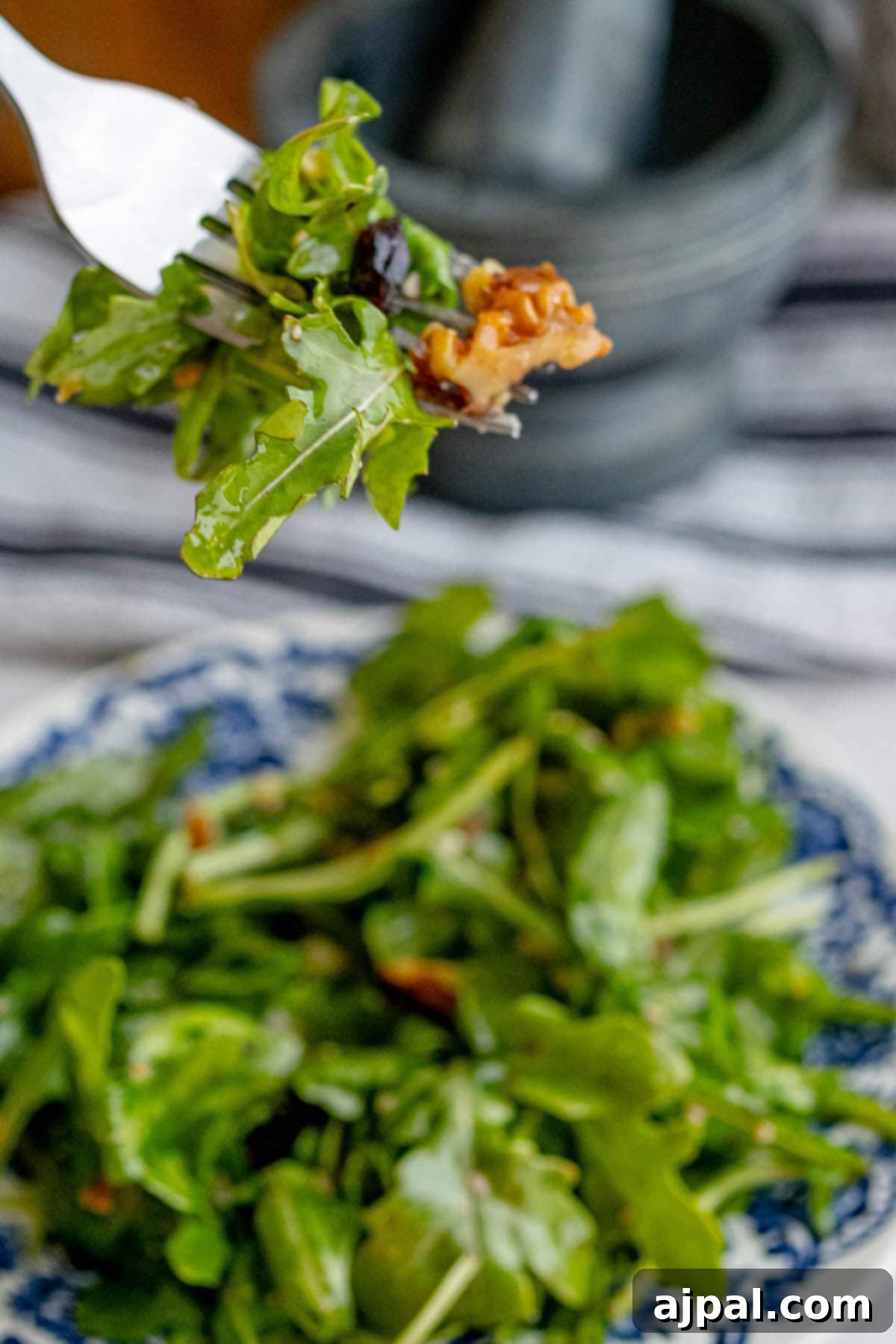 A person is holding a fork over a plate of freshly made Arugula Salad.