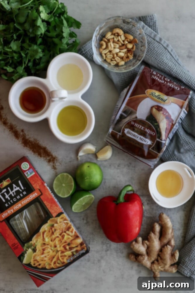 A collection of fresh ingredients for miso noodle salad: miso paste, bell pepper, limes, garlic, ginger, sesame oil, vinegar, and rice noodles.