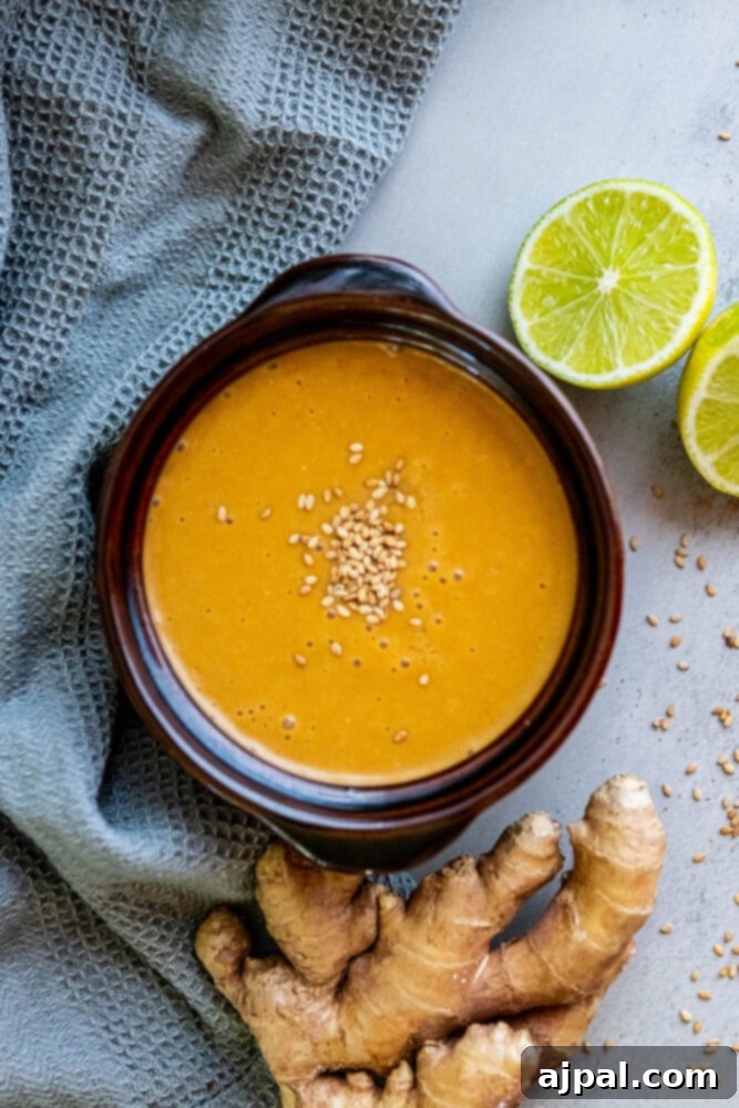 A bowl of vibrant yellow Asian dressing, garnished with fresh lime wedges and sliced ginger, ready for the noodle salad.