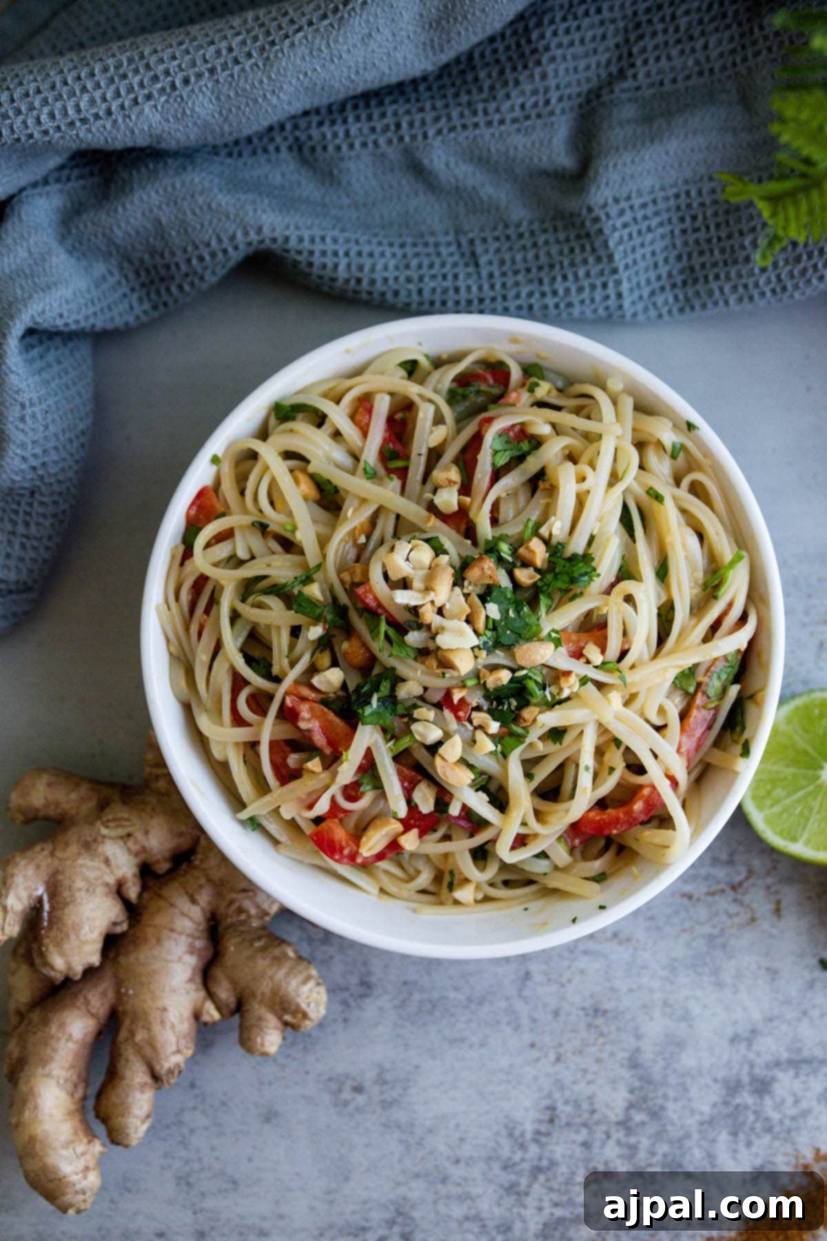A vibrant mix of noodles, bell pepper, and cilantro tossed in a savory sauce, with fresh lime and ginger scattered around.