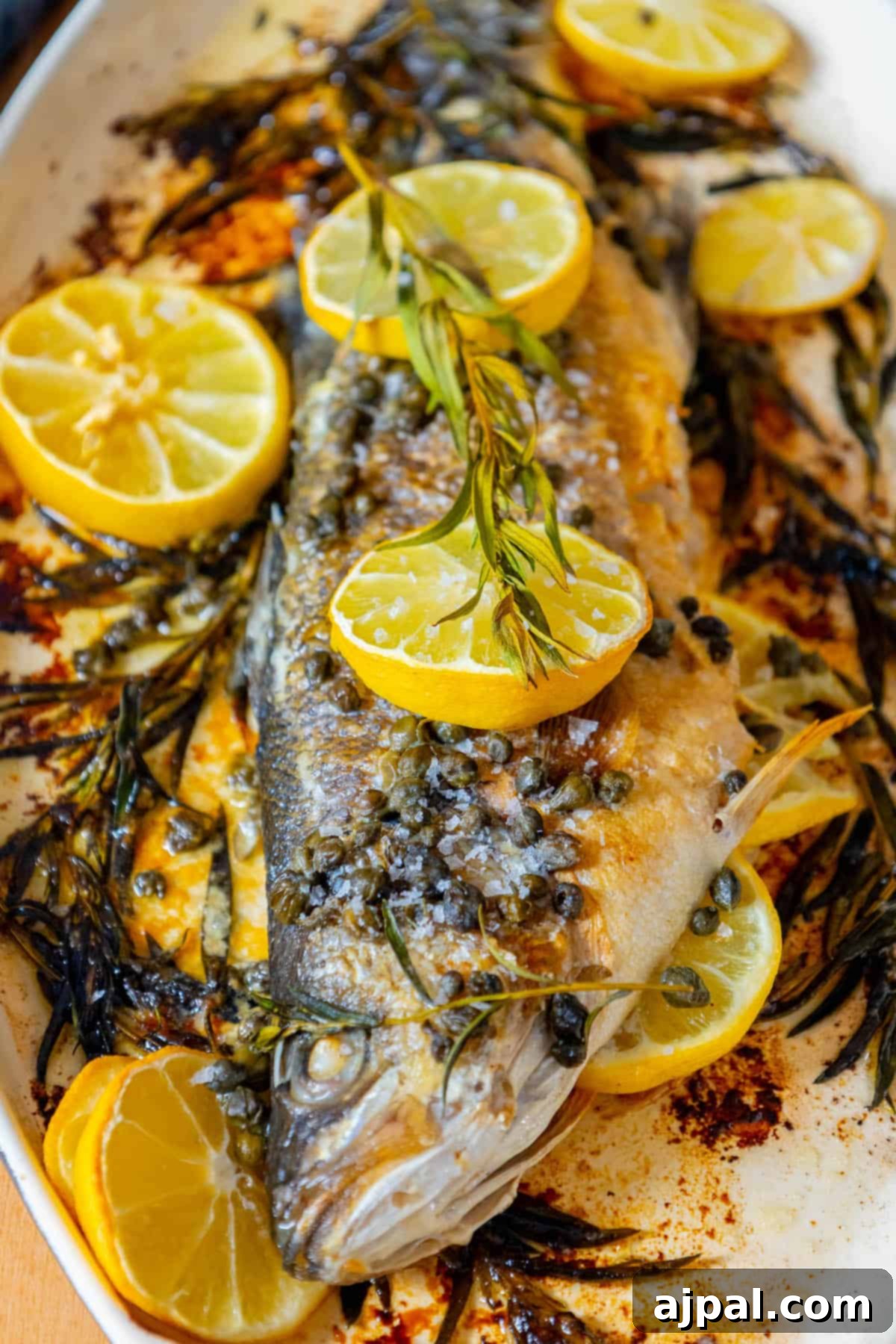 Roasted Branzino with Zesty Lemon-Caper Butter 14 A perfectly roasted Branzino, gracefully served with fresh lemon slices and a scattering of herbs on a clean white plate, creating an inviting presentation.